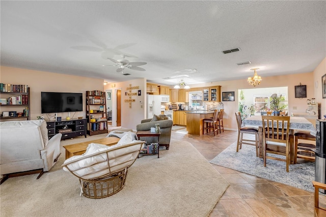 living area featuring visible vents, a textured ceiling, and ceiling fan with notable chandelier