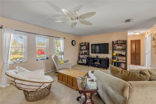 living area featuring a ceiling fan, light colored carpet, visible vents, and a textured ceiling