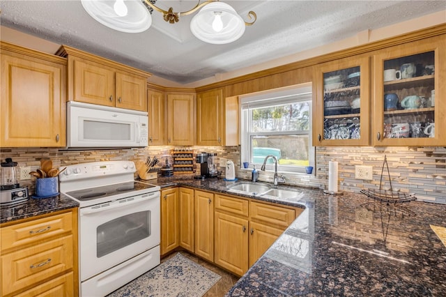 kitchen featuring decorative backsplash, glass insert cabinets, a sink, dark stone counters, and white appliances