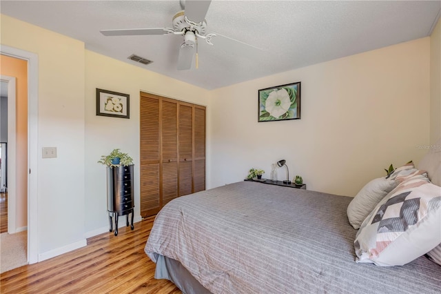 bedroom with baseboards, visible vents, light wood-style flooring, ceiling fan, and a closet