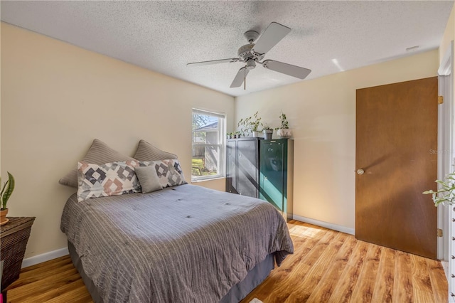 bedroom with ceiling fan, a textured ceiling, baseboards, and wood finished floors