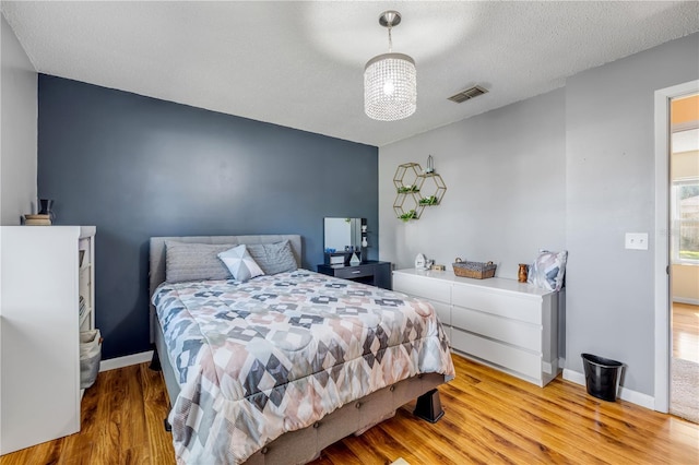 bedroom featuring light wood finished floors, baseboards, visible vents, and a textured ceiling