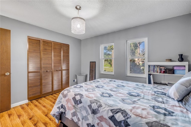 bedroom featuring light wood-style flooring, a textured ceiling, baseboards, and a closet