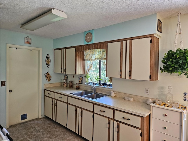 kitchen featuring a textured ceiling, light countertops, a sink, and dark tile patterned flooring