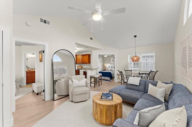 living area featuring high vaulted ceiling, light wood-type flooring, visible vents, and a ceiling fan