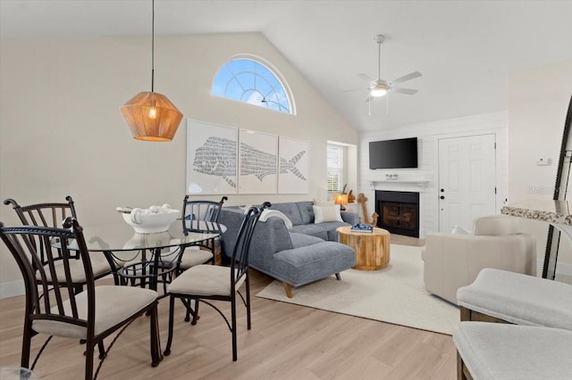 living area with high vaulted ceiling, a fireplace, a ceiling fan, and light wood-style floors