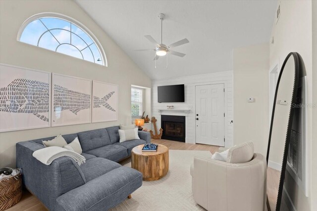 living area featuring a large fireplace, ceiling fan, visible vents, and wood finished floors