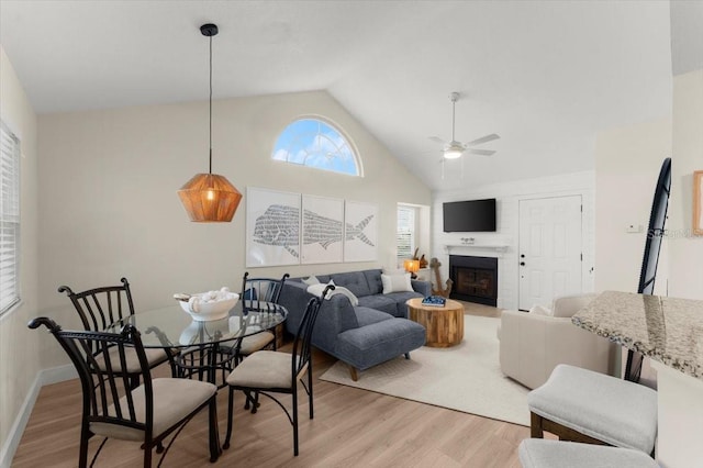 living room featuring a ceiling fan, a large fireplace, high vaulted ceiling, and light wood finished floors