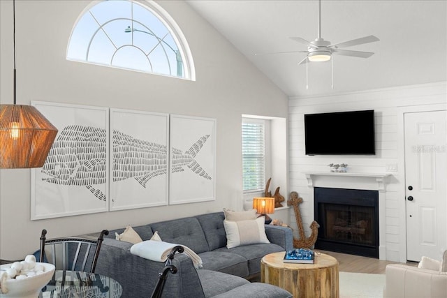 living area featuring a ceiling fan, a large fireplace, high vaulted ceiling, and wood finished floors