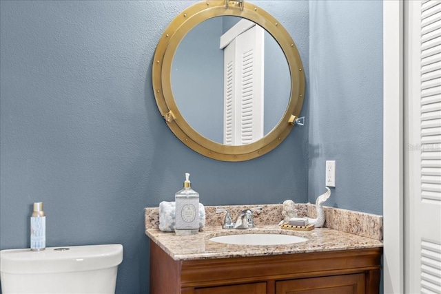 bathroom with a textured wall, vanity, and toilet