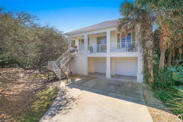 view of front of house featuring driveway, stairway, an attached garage, covered porch, and stucco siding