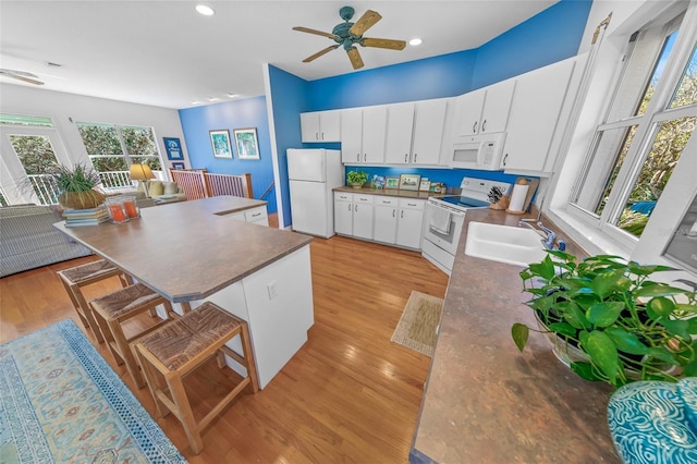 kitchen featuring light wood-style floors, dark countertops, white appliances, and a sink