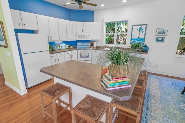 kitchen with white appliances, white cabinets, dark countertops, light wood-style floors, and recessed lighting