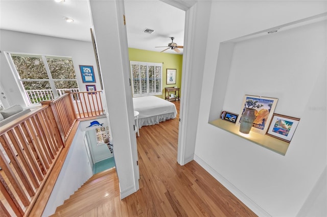 hall featuring baseboards, visible vents, wood finished floors, and an upstairs landing