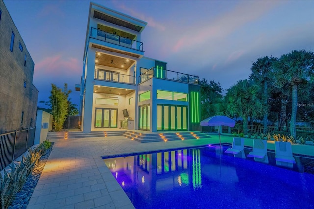 back of house at dusk featuring a fenced in pool, a ceiling fan, a balcony, a patio, and a fenced backyard