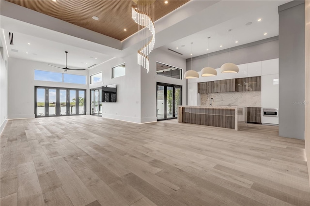 unfurnished living room with french doors, light wood-type flooring, and a towering ceiling