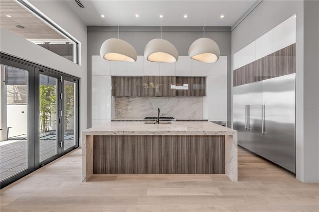 kitchen featuring a high ceiling, a sink, white cabinetry, backsplash, and modern cabinets