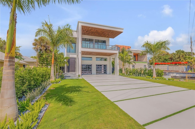 view of front of property with stucco siding, concrete driveway, a balcony, a garage, and a front lawn