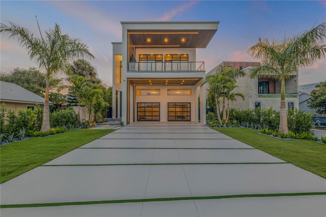 contemporary home with a balcony, a garage, driveway, stucco siding, and a front lawn