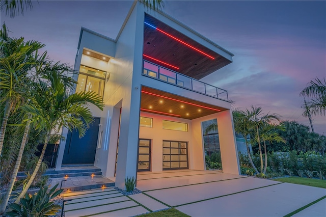 exterior entry at dusk with a balcony and stucco siding