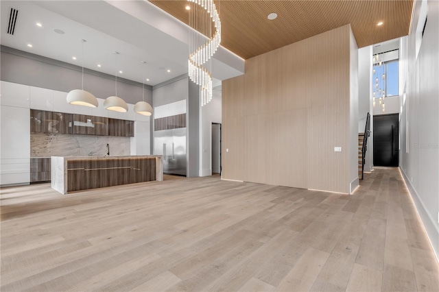 unfurnished living room with light wood-type flooring, visible vents, a sink, and a high ceiling