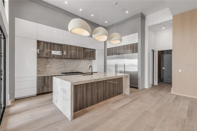 kitchen featuring light wood finished floors, a high ceiling, modern cabinets, and a sink