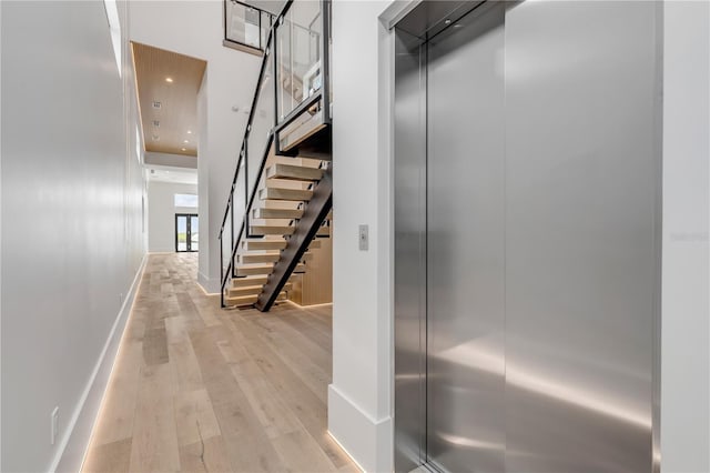 hall with a high ceiling, baseboards, light wood-style floors, stairway, and elevator