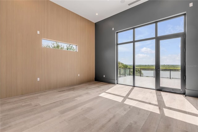 empty room with a water view, light wood-style floors, a high ceiling, and visible vents