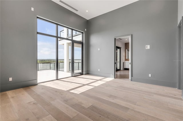 empty room with a high ceiling, visible vents, light wood-style flooring, and baseboards