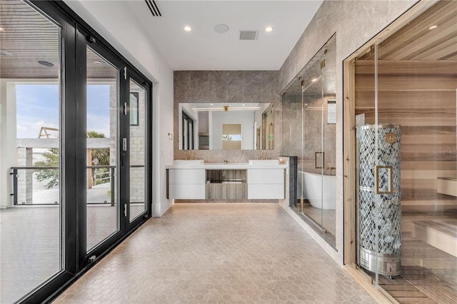 bathroom featuring tile walls, a soaking tub, visible vents, and vanity