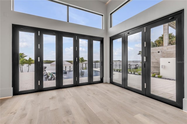 unfurnished room featuring wood finished floors, a water view, french doors, and a towering ceiling