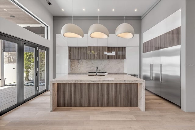 kitchen featuring modern cabinets, built in refrigerator, a towering ceiling, light wood-style flooring, and white cabinets