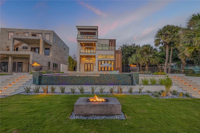 back of house at dusk with stairs, an outdoor fire pit, a balcony, and a lawn