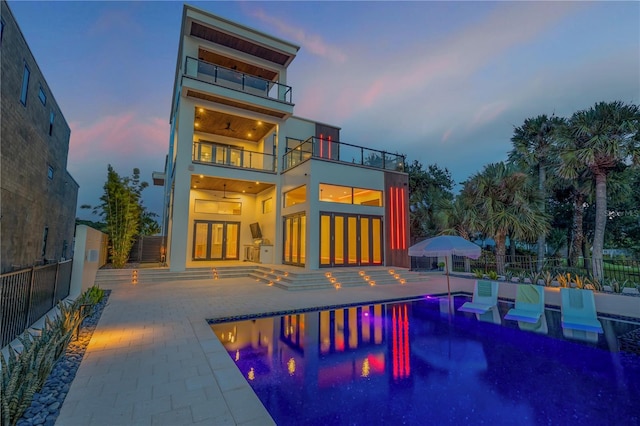 back of house at dusk featuring a balcony, fence, a patio area, and ceiling fan