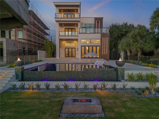 back of property at dusk featuring an outdoor fire pit, a balcony, stucco siding, stairway, and a patio area