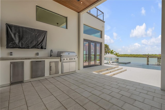 view of patio / terrace featuring an outdoor kitchen, grilling area, french doors, a water view, and a sink