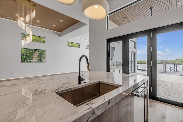 kitchen with a sink, recessed lighting, hanging light fixtures, light stone counters, and a water view
