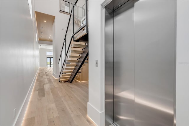 hall featuring light wood-type flooring, stairway, baseboards, recessed lighting, and a towering ceiling
