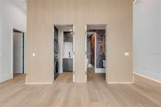 unfurnished bedroom featuring stacked washer and clothes dryer, light wood-style flooring, a spacious closet, a closet, and baseboards