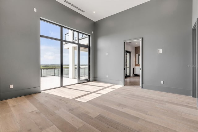 unfurnished room with a high ceiling, light wood finished floors, baseboards, and a water view