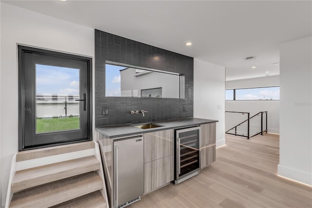 indoor bar featuring wine cooler, stainless steel built in fridge, backsplash, baseboards, and light wood finished floors