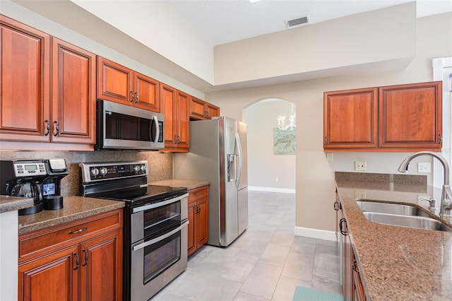 kitchen with dark stone counters, arched walkways, a sink, stainless steel appliances, and backsplash