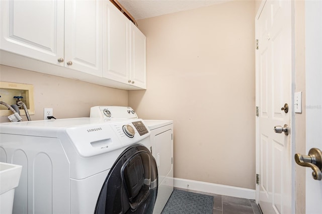 washroom featuring baseboards, cabinet space, separate washer and dryer, and dark tile patterned flooring