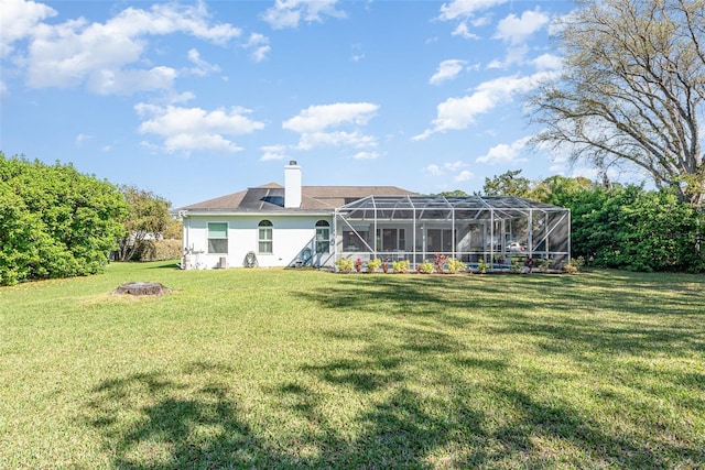 back of house with glass enclosure, a chimney, a lawn, and stucco siding