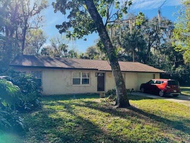 ranch-style home with stucco siding, an attached garage, driveway, and a front lawn