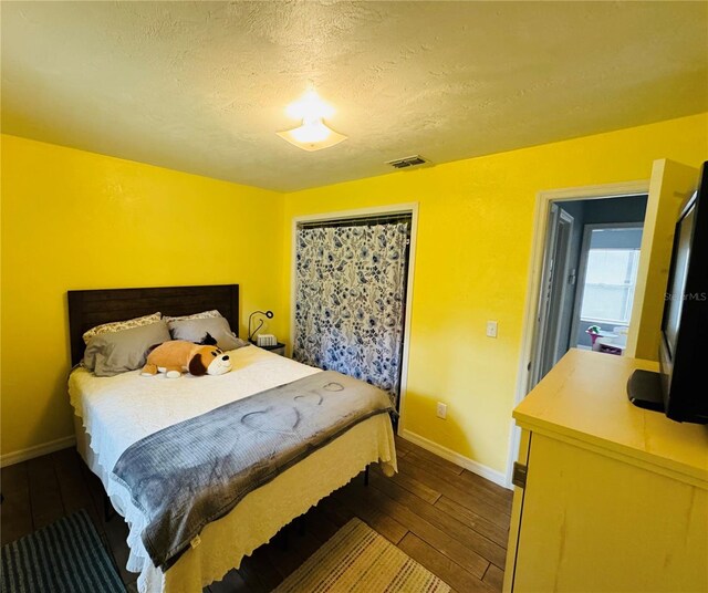 bedroom with visible vents, a textured ceiling, baseboards, and dark wood-style flooring