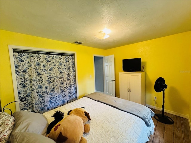 bedroom featuring a textured ceiling, wood finished floors, visible vents, and baseboards