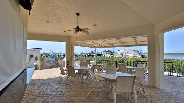 view of patio featuring fence, exterior kitchen, a water view, outdoor dining space, and a ceiling fan