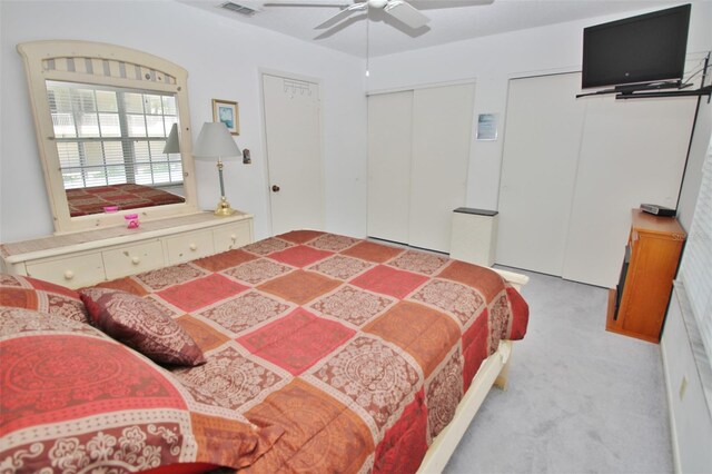 carpeted bedroom featuring visible vents, multiple closets, and a ceiling fan