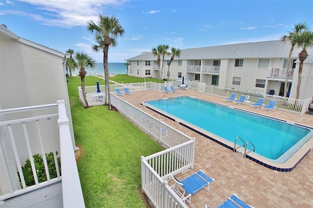 community pool featuring a patio, a lawn, fence, and a water view